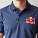 Gros plan sur le torse d'une personne portant un polo Red Bull bleu marine texturé, avec le logo emblématique sur la poitrine.